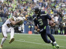 Seattle Seahawks QB Russell Wilson, seen here being chased by a New Orleans Saints defender in a game at CenturyLink Field, indicated heâ€™d waive his no trade clause for four potential teams. (Image: Ted S. Warren/AP)